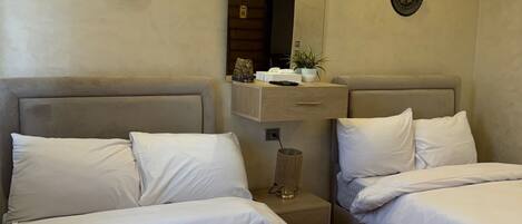 Habitación de hotel con dos camas, una mesita de noche, un espejo y una lámpara fijada a la pared.