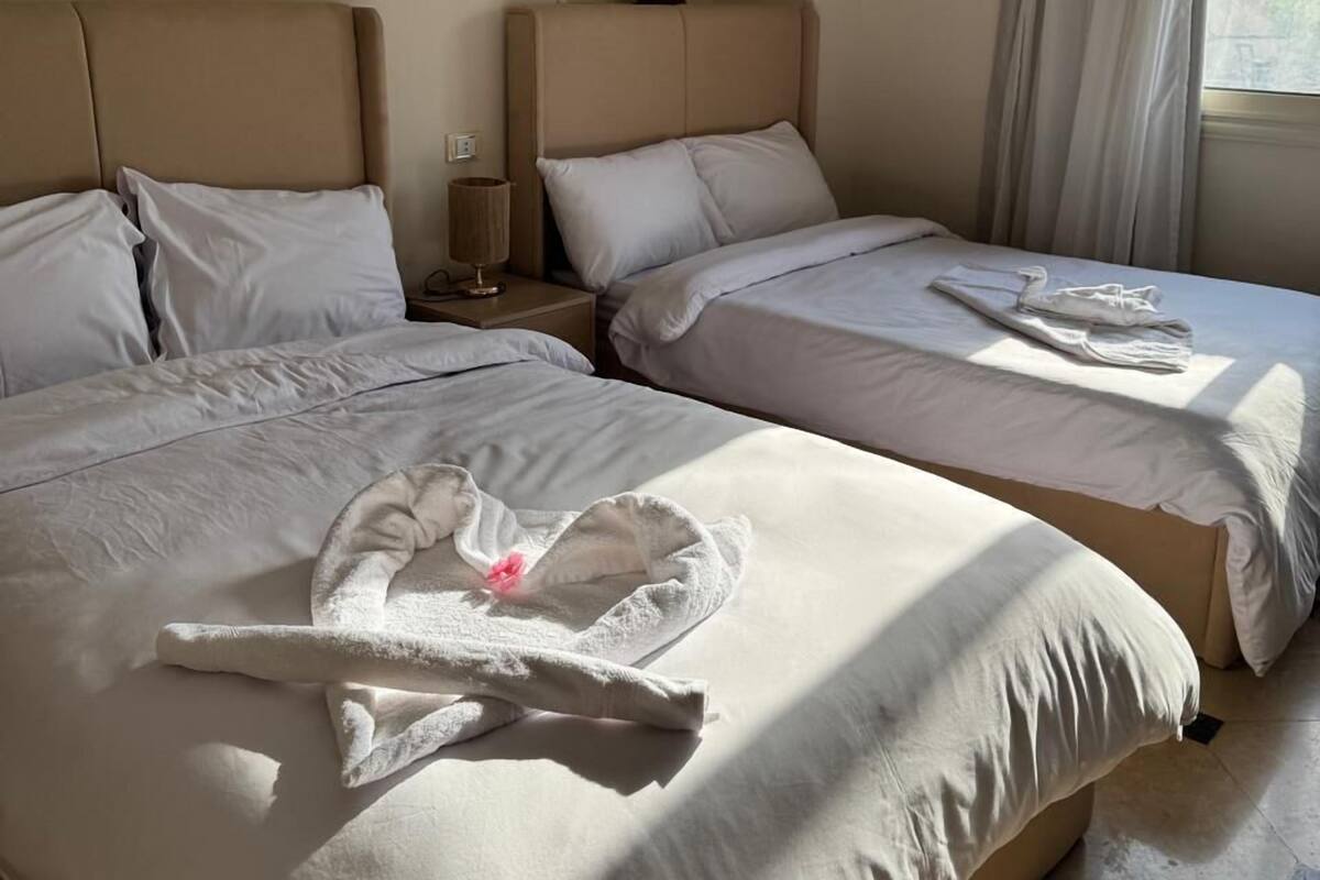 Hotellihuone, jossa on kaksi sänkyä, yöpöytä, lamppu ja ikkuna, jossa on verhot.