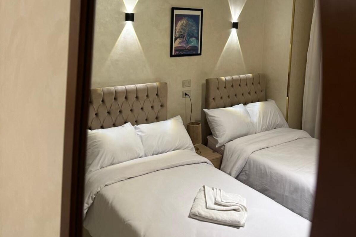 Une chambre d’hôtel avec deux lits, un tableau au mur et deux lampes fixées au mur.