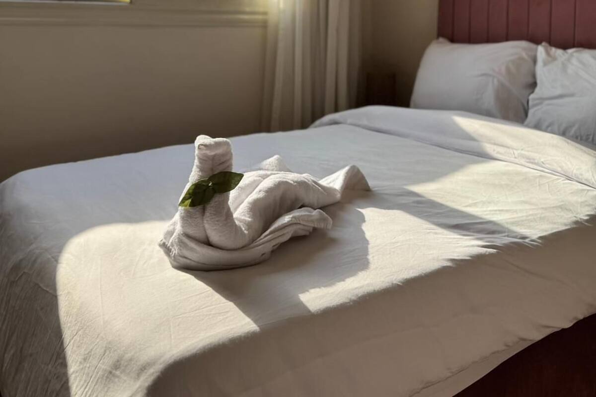Hotellihuone, jossa on sänky, ikkuna verhoilla, ilmastointilaite ja näkymä pyramidiin.