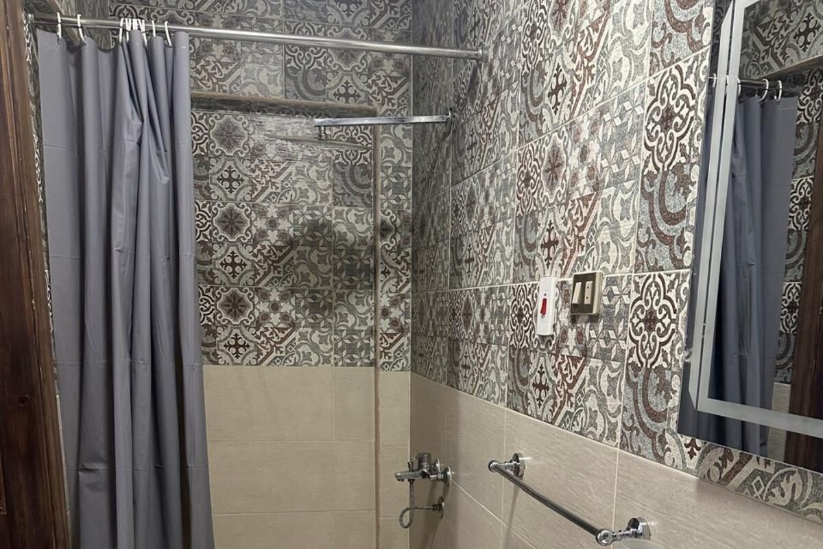 A bathroom with patterned tiles, a shower with a glass door, a sink with a mirror, and a towel rack.