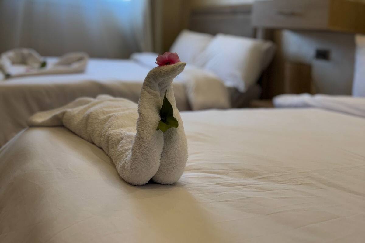 Hotellihuone, jossa on kaksi sänkyä, yöpöytä, seinäkello ja ikkuna, jossa on verhot.