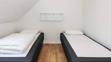 A small, single-room accommodation with two beds, a wooden floor, and a sloped ceiling.