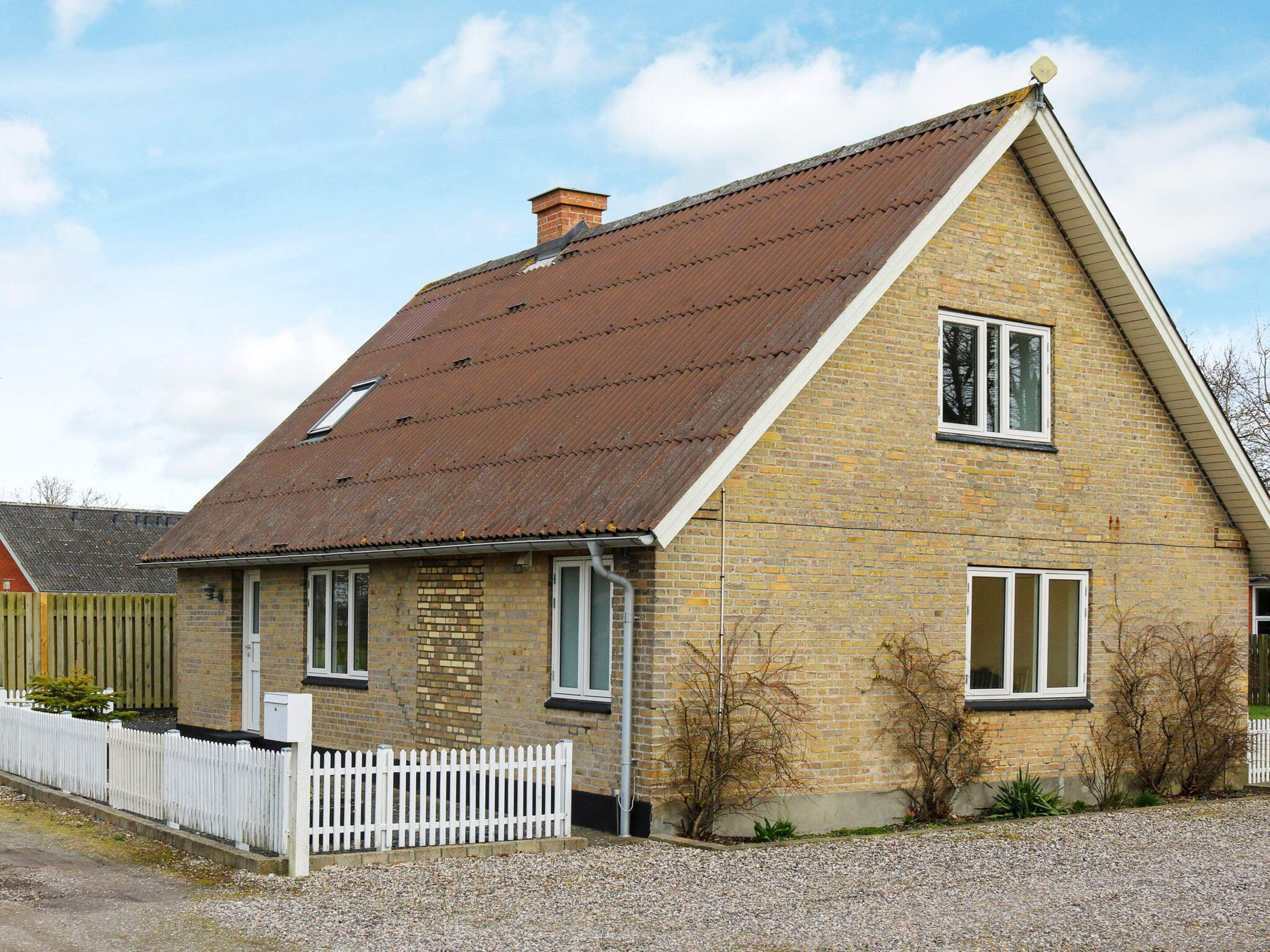 A two-story house with a sloped roof, a white picket fence, and a gravel driveway.