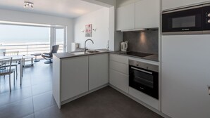 A modern kitchen with white cabinets, a Bosch microwave, and a large window overlooking the sea. - Apartment on Sea Wall With Stunning Views (Koksijde)
