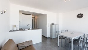 A modern kitchen with a built-in sink and a dining area with a white table and chairs. - Apartment on Sea Wall With Stunning Views (Koksijde)