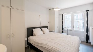 A bedroom with a bed, a wardrobe, a window with curtains, and a radiator. - Apartment on Sea Wall With Stunning Views (Koksijde)