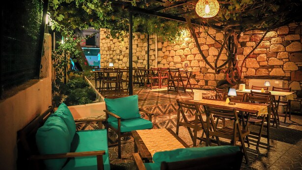 Ein Straßencafé mit Steinwänden, Holztischen und hängenden Weinreben.