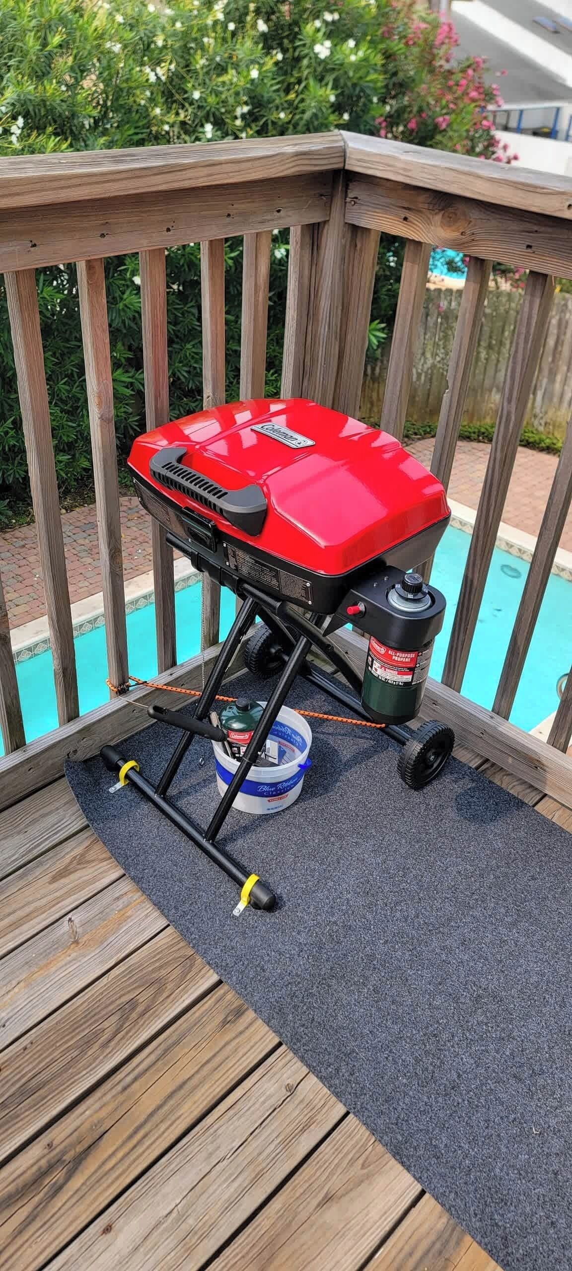 A barbecue grill on a wooden deck with a pool in the background.