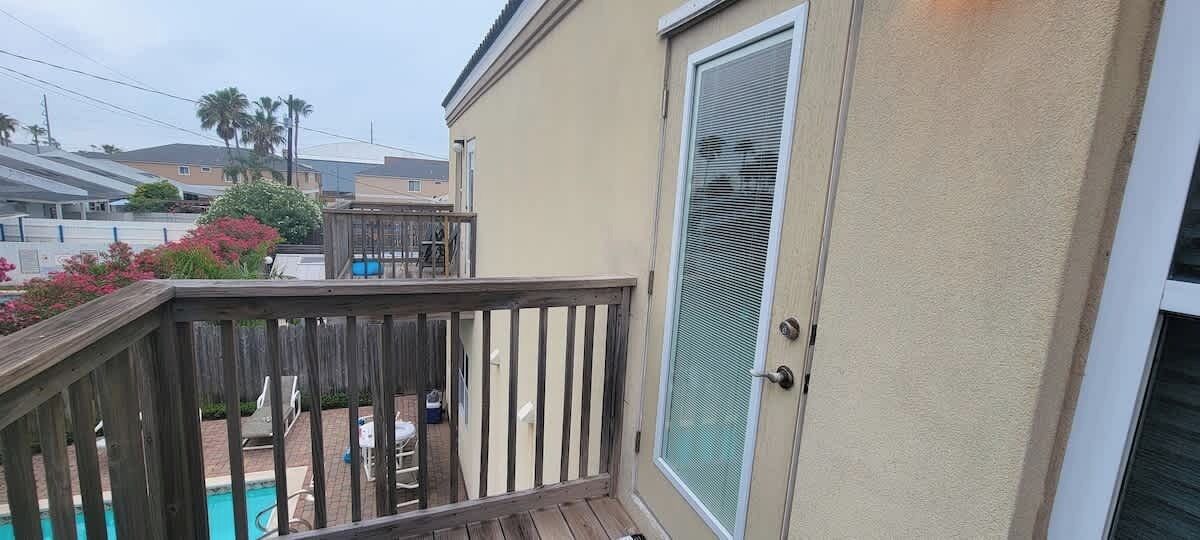 Un immeuble résidentiel doté d’une terrasse en bois, d’une porte-fenêtre coulissante et d’une piscine en arrière-plan.