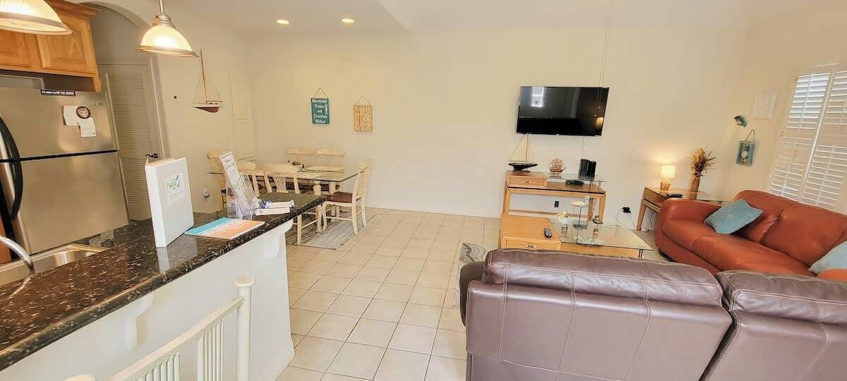 Una cocina moderna con refrigerador, estufa y comedor. Hay un televisor de pantalla plana en la pared y un sofá de cuero en la sala.