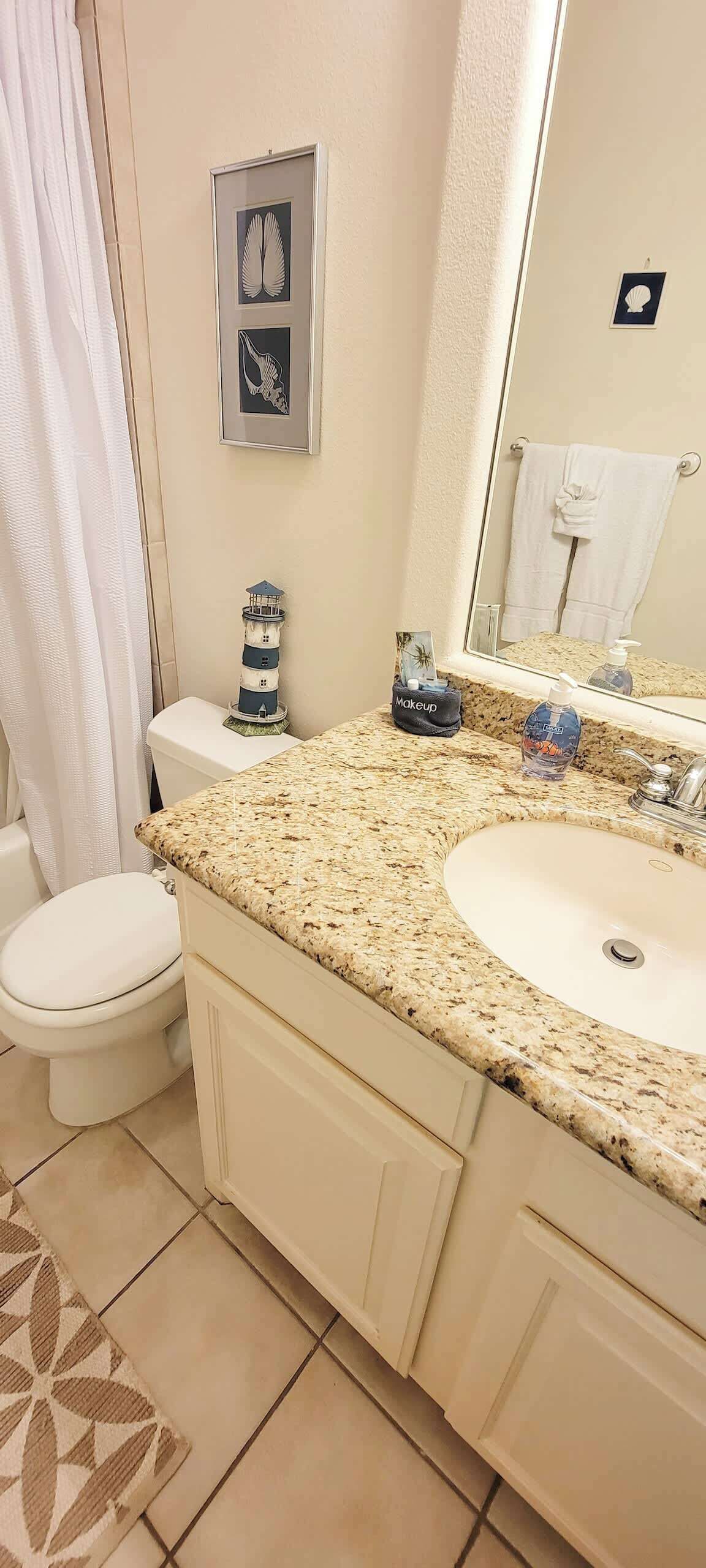 Une salle de bain avec un lavabo encastré dans un plan de toilette en granit, des toilettes et une œuvre d’art encadrée au-dessus du miroir.