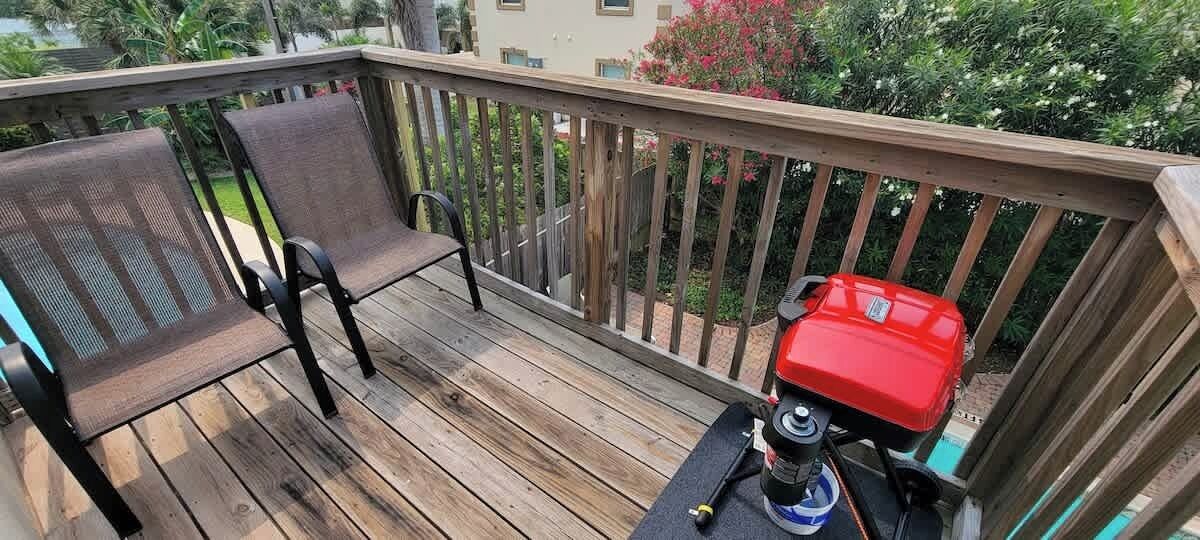 A wooden deck with two chairs and a red grill.