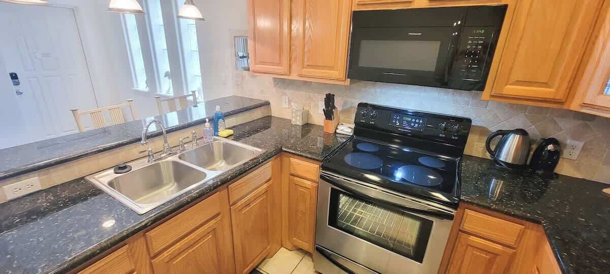 Una cocina con armarios de madera, un lavamanos de acero inoxidable, un microondas negro y una estufa.