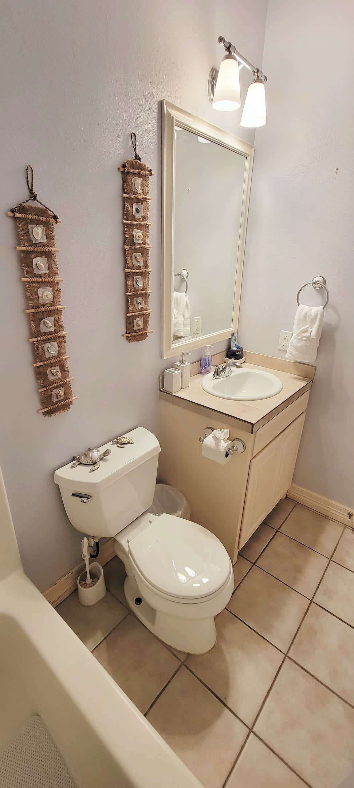 A bathroom with a toilet, sink, mirror, towel rack, and a wall-mounted towel rack.