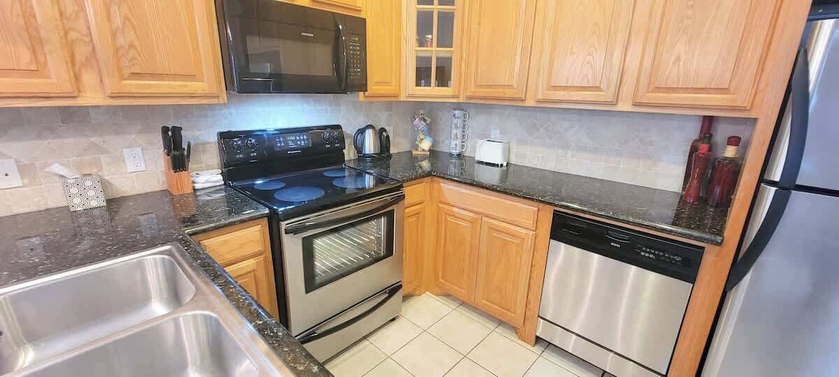 Una cocina moderna con armarios de madera, un refrigerador de acero inoxidable, un lavavajillas, una estufa y un microondas.