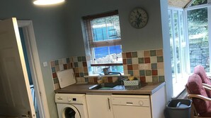 Une cuisine compacte équipée d’un lave-linge, d’un évier et d’une fenêtre avec des stores.