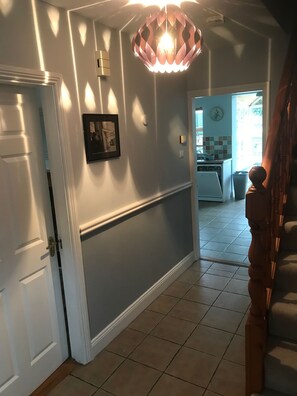 A hallway with a white door, a framed picture on the wall, and a kitchen visible through an open door. - Comfortable Baltimore Home With Modern Amenities Ideal for Families (Baltimore)