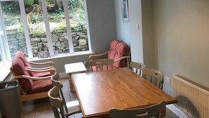 Un coin repas avec une table et des chaises en bois, une fenêtre donnant sur un paysage verdoyant et un radiateur au mur.