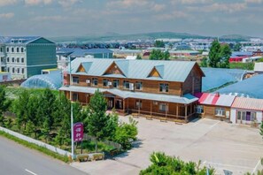 A two-story building with a wooden facade and a green roof, surrounded by trees and a parking lot. - Erguna Yinuoyi Hotel (Ergun)