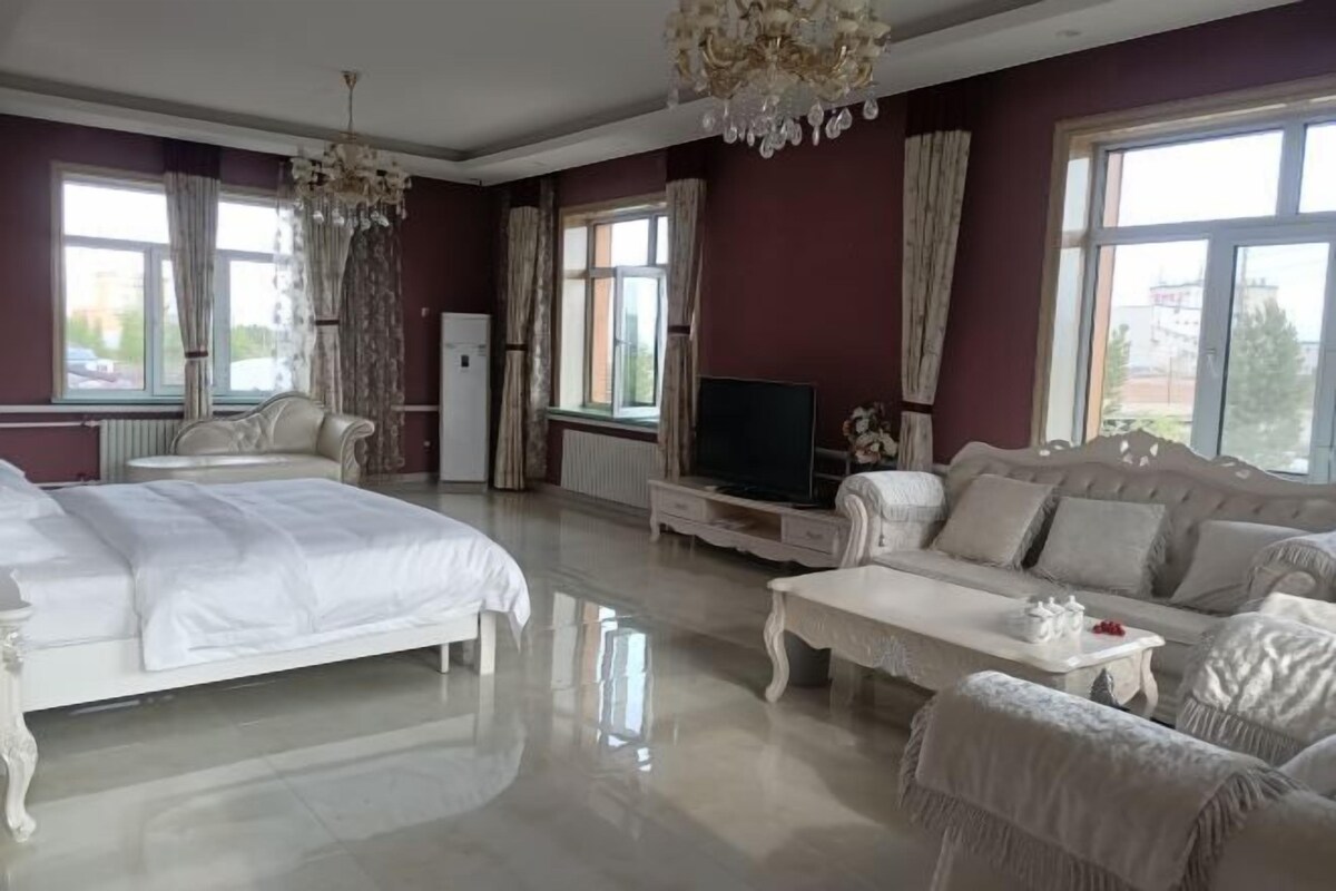 A spacious bedroom with a large bed, a sofa, a TV, and a chandelier.