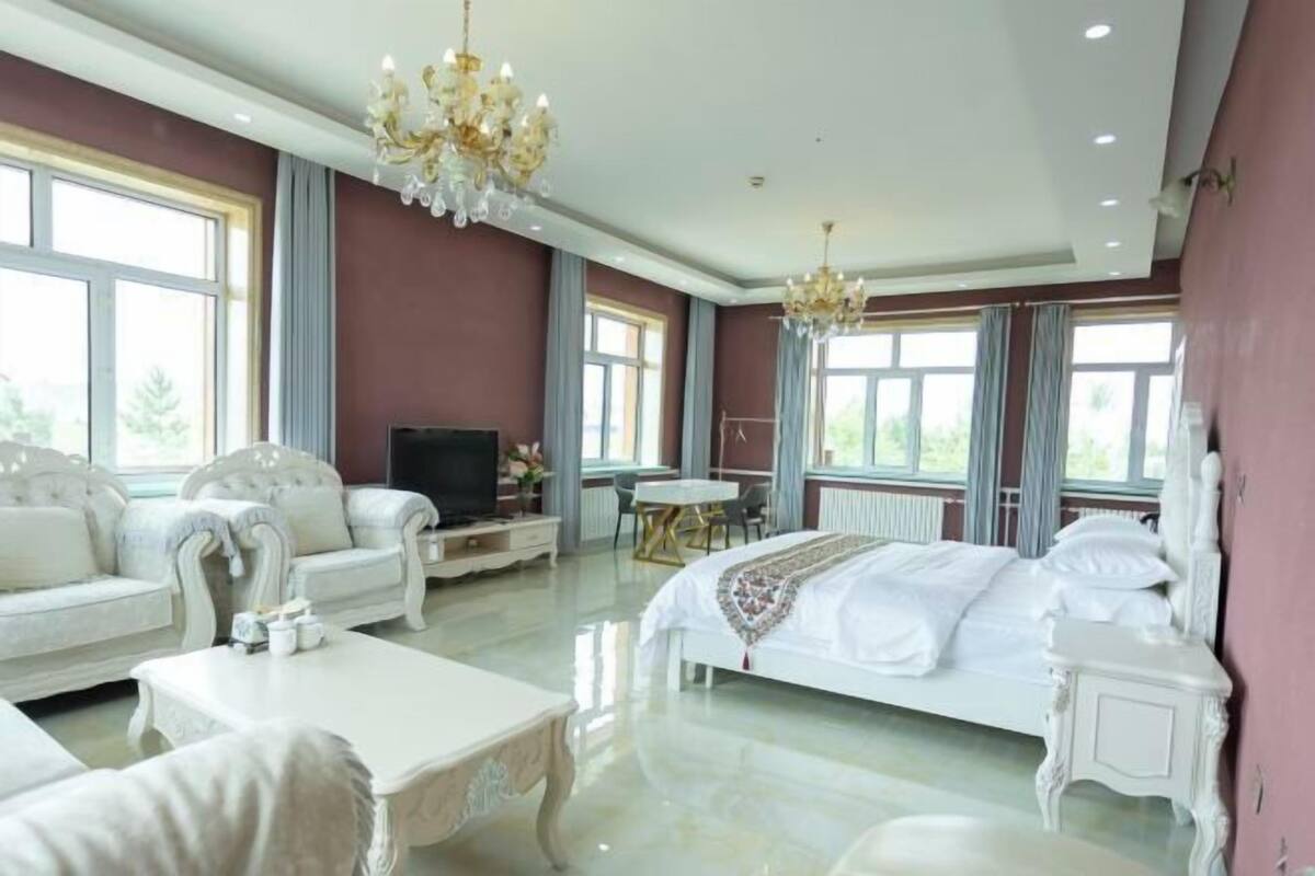 Quarto de hotel espaçoso com uma cama grande, área de estar com sofá e poltronas, televisão e uma mesa de jantar.
