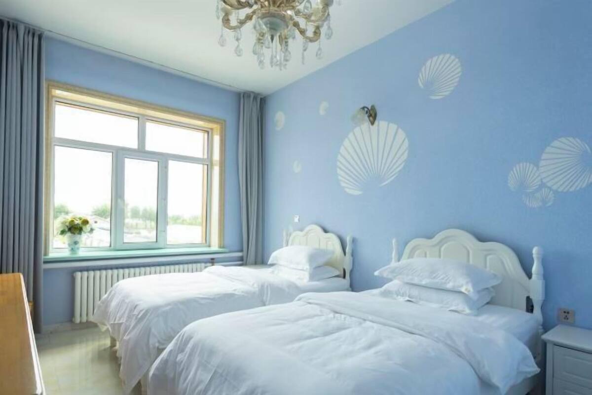 Quarto com duas camas, janela com cortinas, candelabro e conchas decorativas na parede.