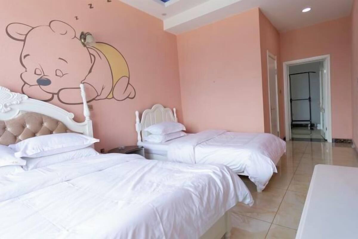 Quarto com duas camas, decoração de urso de pelúcia na parede e cabeceira branca.
