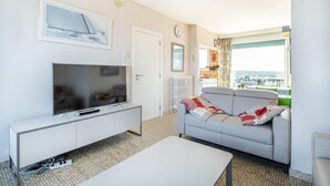 Ein modernes Wohnzimmer mit Flachbildfernseher, einer Couch, einem Couchtisch und Blick auf die Stadt durch große Fenster.