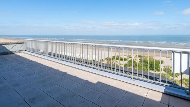 Ein Balkon mit Metallgeländer, der auf einen Strand blickt.