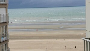 Blick auf einen Strand von einem Gebäude mit Balkonen, das auf eine Sandküste und das Meer unter einem bewölkten Himmel blickt.