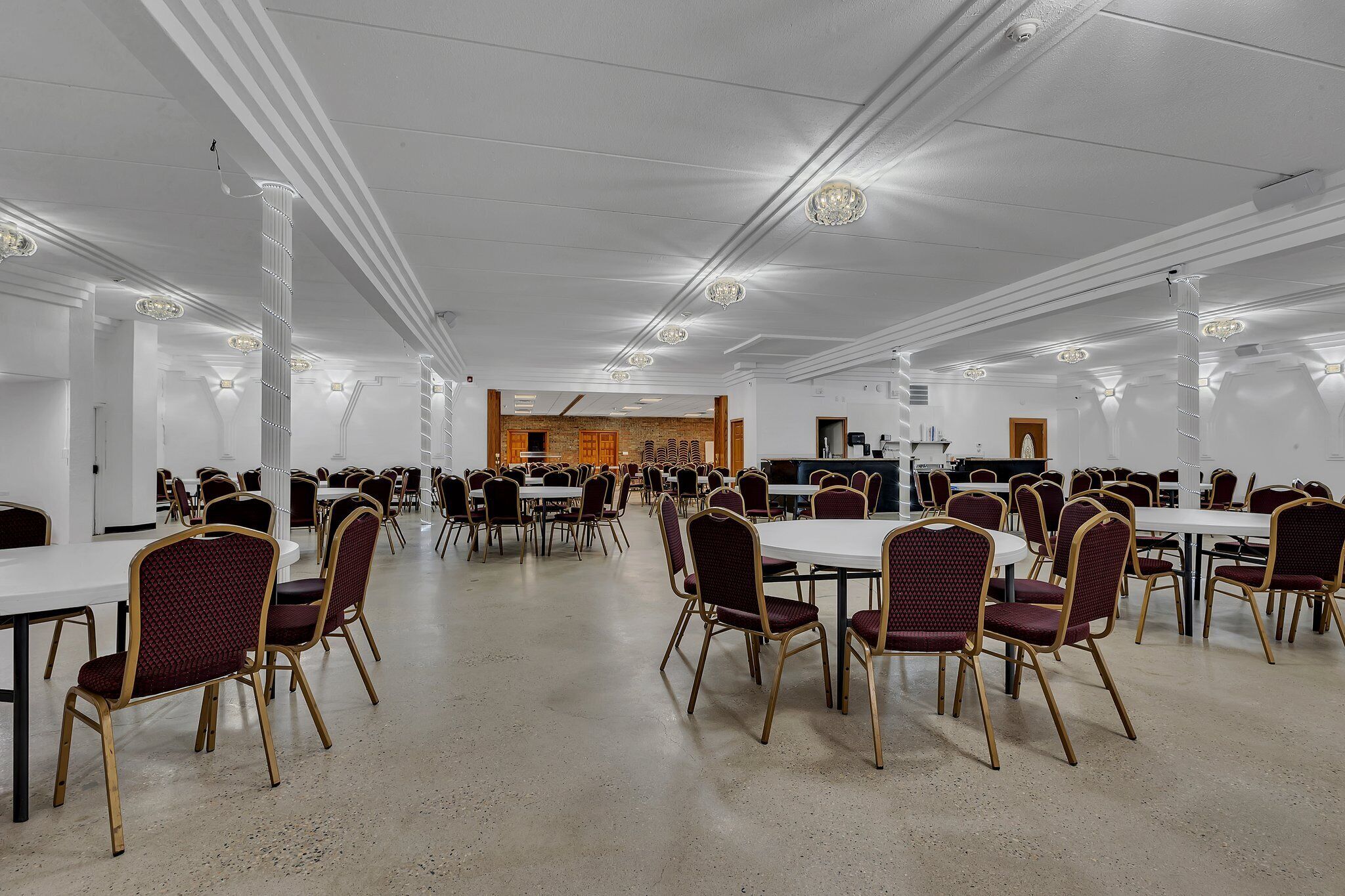 Un'ampia sala conferenze con numerosi tavoli e sedie, pareti bianche e luci a soffitto.