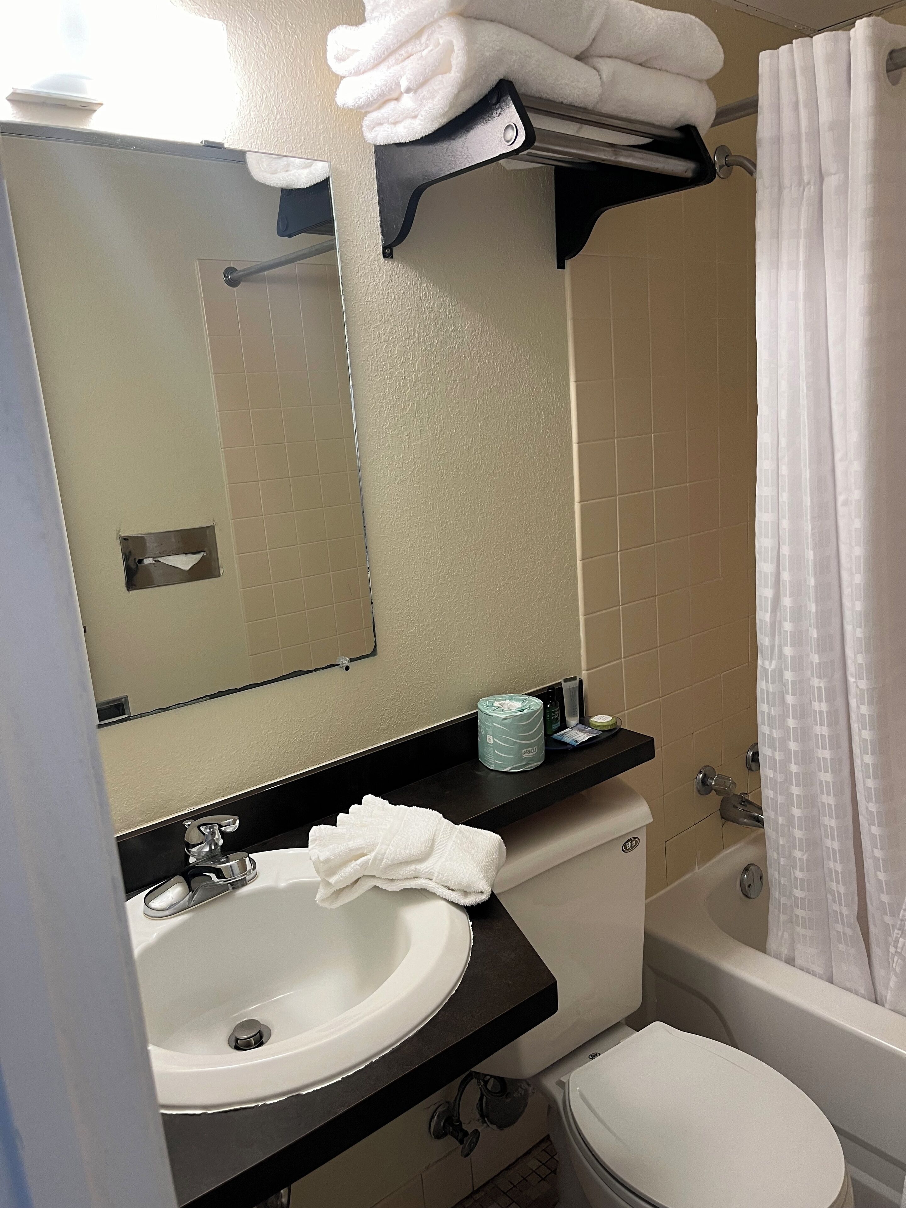 A bathroom with a sink, toilet, and bathtub. There is a towel rack with folded towels, a mirror, and a shelf with toiletries.