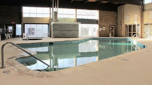 An indoor swimming pool with clear water, a metal ladder, and a view of the outside through large windows. - The Hudson Inn (Morris)