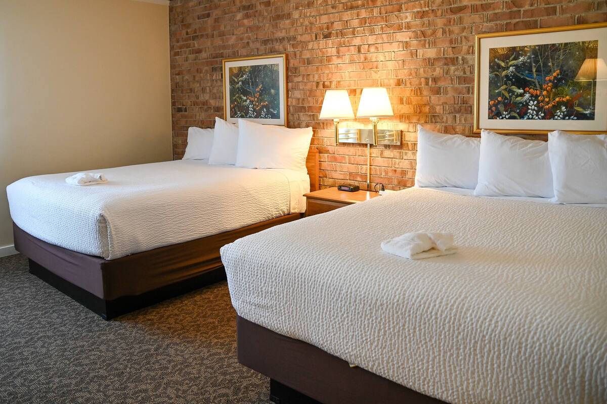 A hotel room with two beds, a brick wall, and two framed pictures.