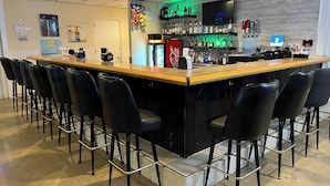 A bar area with a long counter, black bar stools, and a variety of liquor bottles. - The Hudson Inn (Morris)