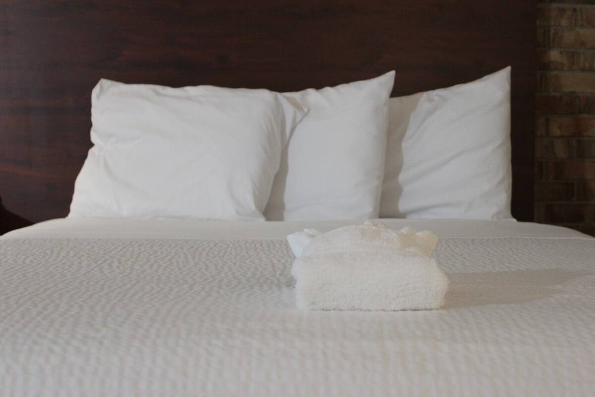 A neatly made bed with white bedding and pillows, a brick wall behind, and a wooden headboard.