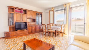 A living room with a TV, wooden cabinets, a dining table with chairs, and a sofa. - Tra Cielo e Terra - Italian Homing (Desenzano del Garda)