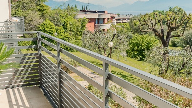 A balcony with a view of a mountainous landscape, trees, and a building in the background. - Tra Cielo e Terra - Italian Homing (Desenzano del Garda)