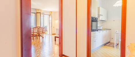 A hallway leading to a dining area with patterned flooring and a view of a kitchen with white cabinets and a tiled backsplash.