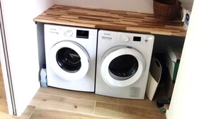 A compact laundry area with two front-loading washing machines and a wooden shelf above.