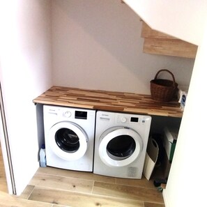 A compact laundry area with two front-loading washing machines and a wooden shelf above.