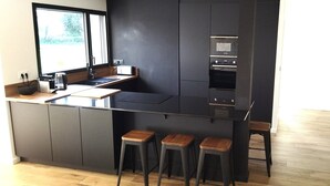 A modern kitchen with dark cabinetry, a built-in oven, and a window providing natural light.