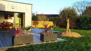 A modern house with a wooden deck, a dining area, and a garden with potted plants.