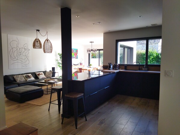 Eine moderne Küche mit einer großen Kochinsel, Holzböden und einem Essbereich mit einer Couch und Stühlen.