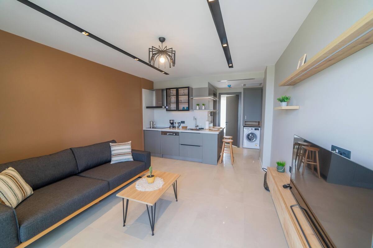 A modern living room with a sofa, coffee table, and a kitchen in the background.