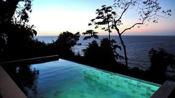 An infinity pool with a view of the ocean at sunset.