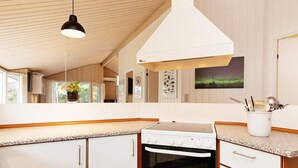 Een keuken met witte kasten, een fornuis en een magnetron. Er is een raam met uitzicht op groen.