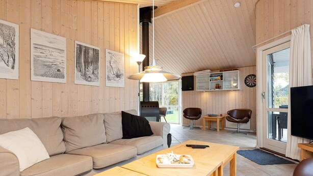 Een gezellige woonkamer met een bank, een houten salontafel en een televisie. Er hangen ingelijste foto's aan de muur, is een open haard en een deur die naar buiten leidt.