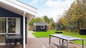 Een modern huis met een terras, een klein speelhuisje en een schommel.
